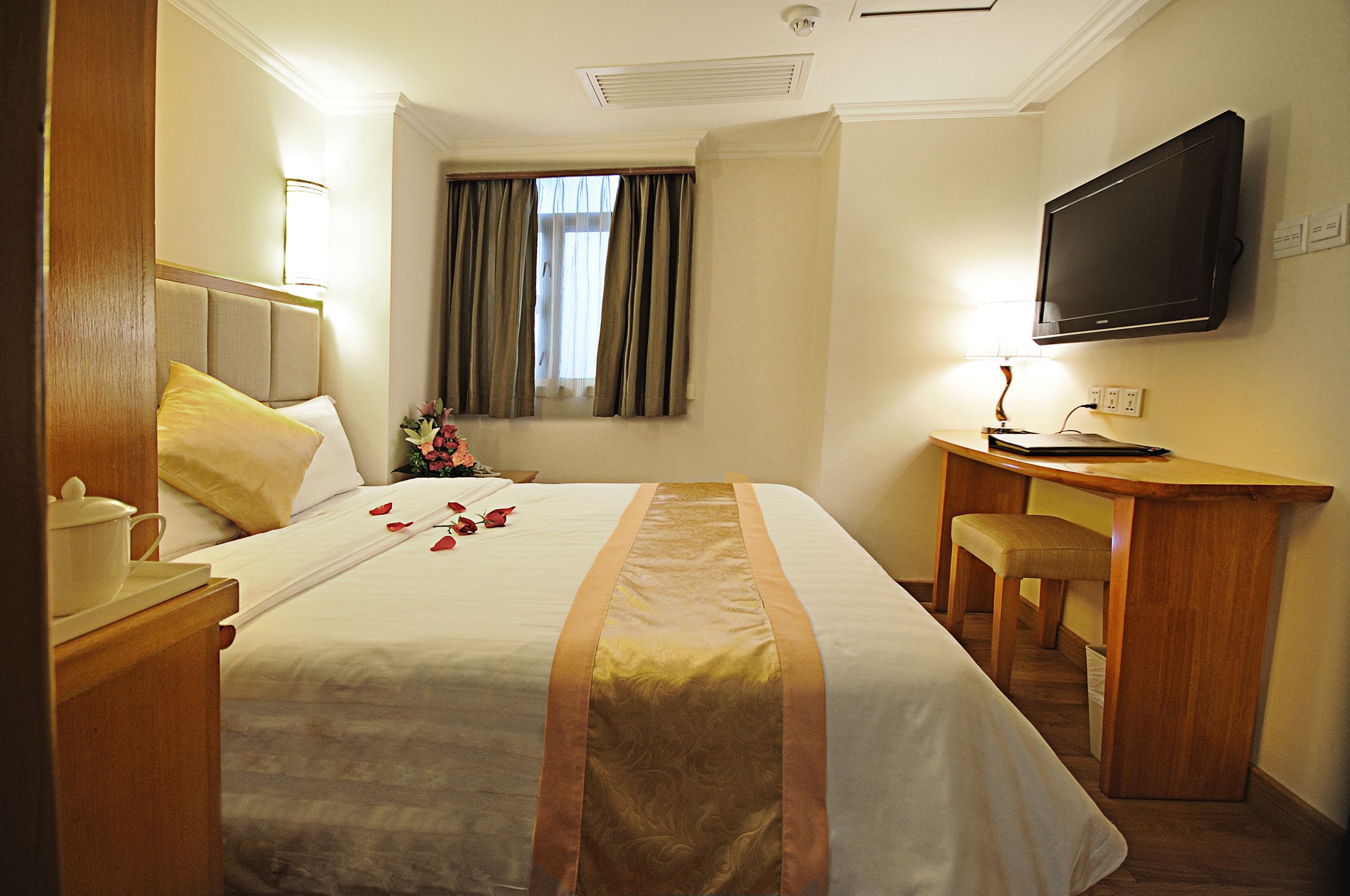Een hotelkamer met een bed, een bureau, een televisie en een raam met gordijnen.