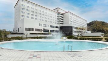 Een modern hotel met een zwembad, een fontein en een bergachtige achtergrond.