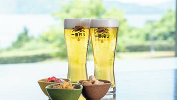 Dos vasos altos de cerveza con un logotipo de tigre, un tazón verde con bocadillos y un tazón marrón con más bocadillos sobre una superficie reflectante.
