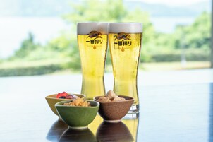 Dos vasos altos de cerveza con un logotipo de tigre, un tazón verde con bocadillos y un tazón marrón con más bocadillos sobre una superficie reflectante.