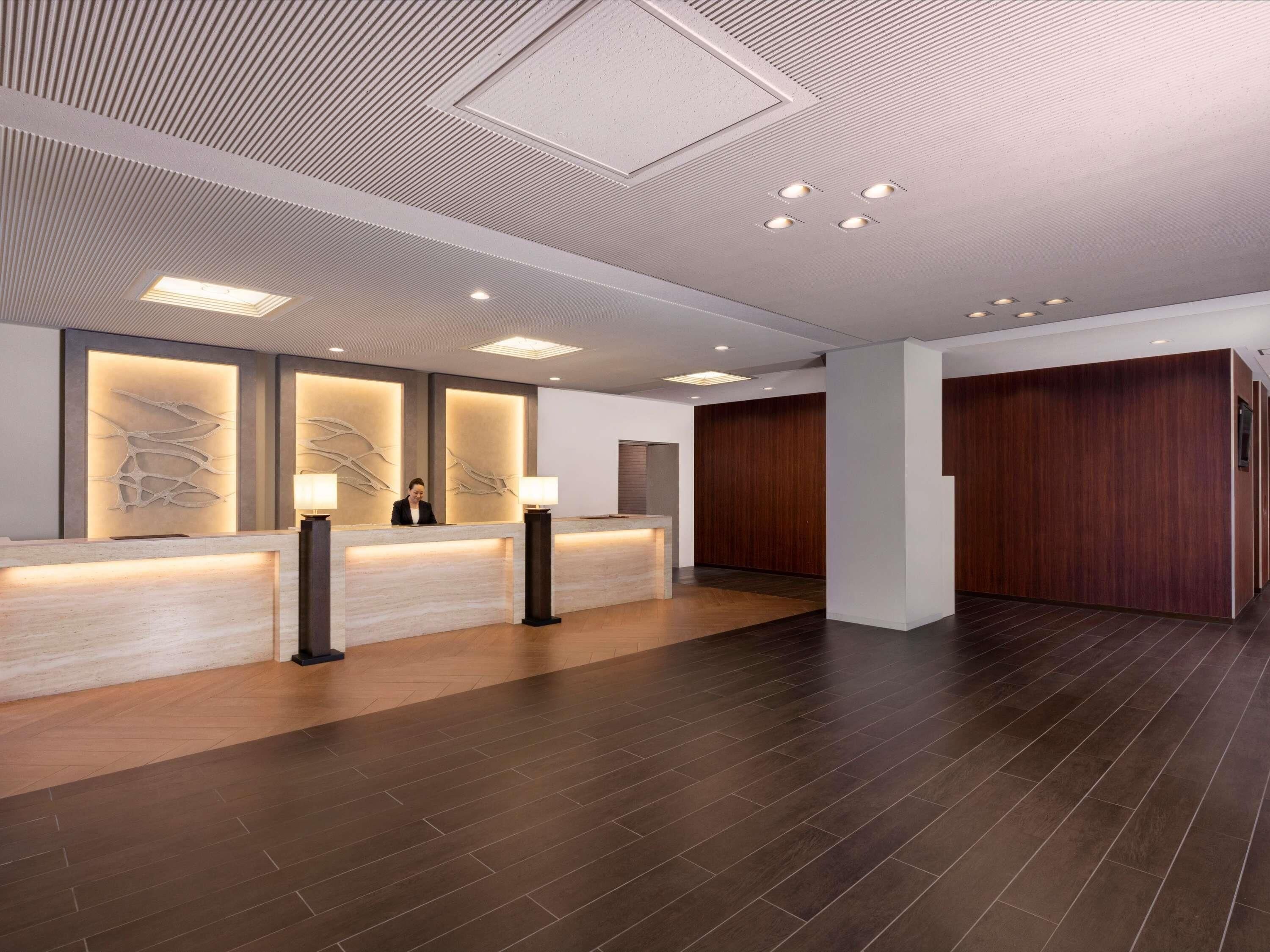 A reception area with a modern design, featuring a reception desk, wall-mounted lamps, and a wooden panel wall.