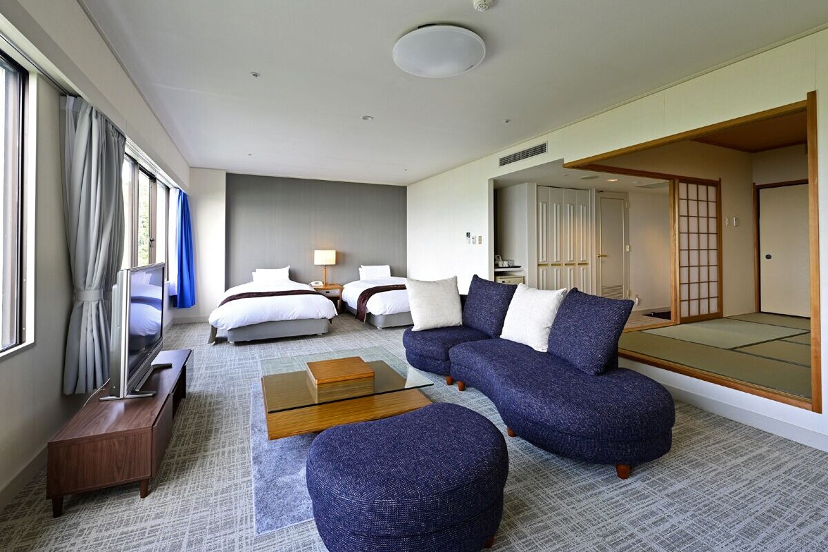 Ein modernes Hotelzimmer mit einem großen Bett, einer Couch, einem Fernseher und einer traditionellen japanischen Schiebetür.