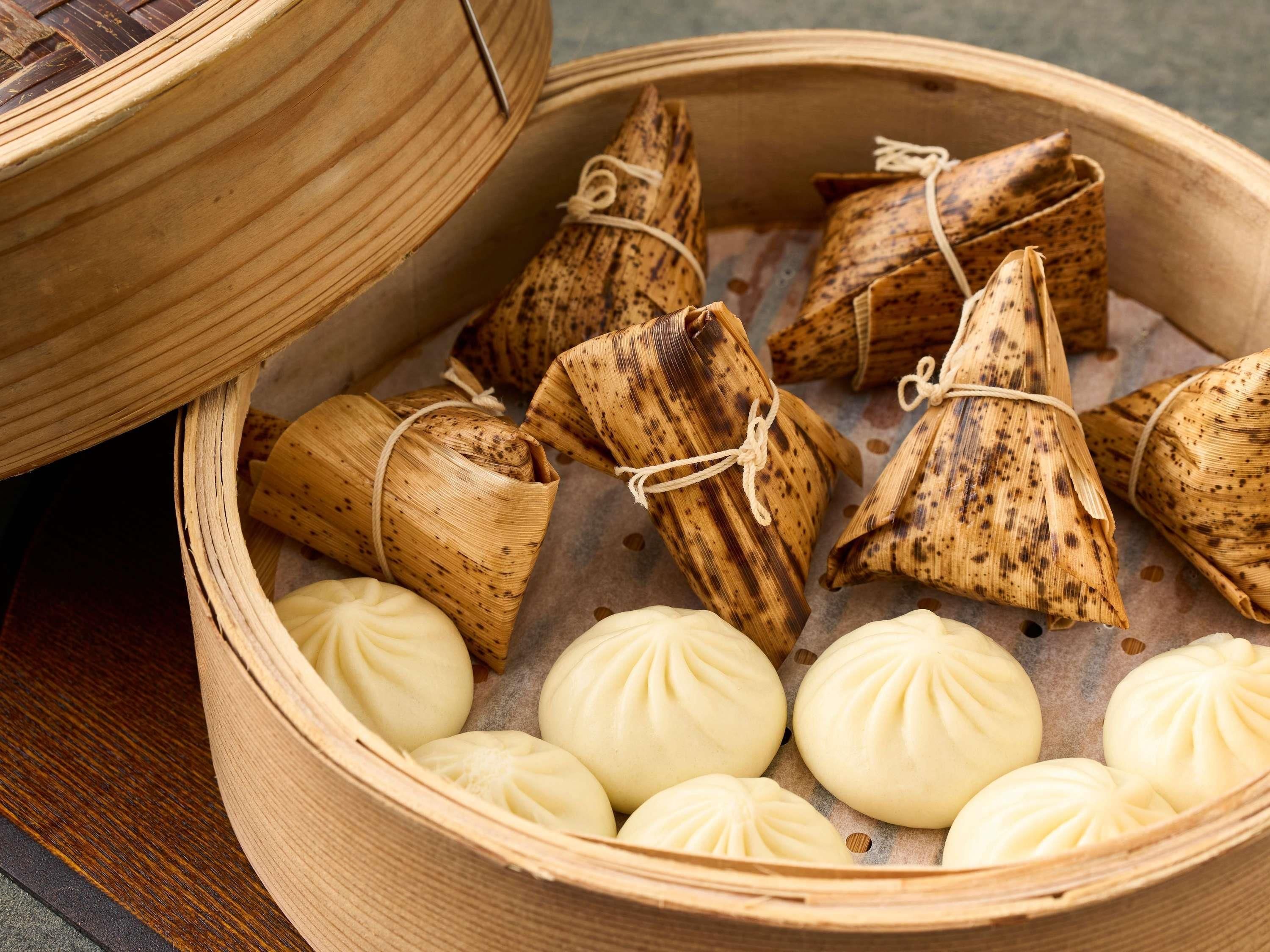 A bamboo steamer with several steamed buns and a covered container.