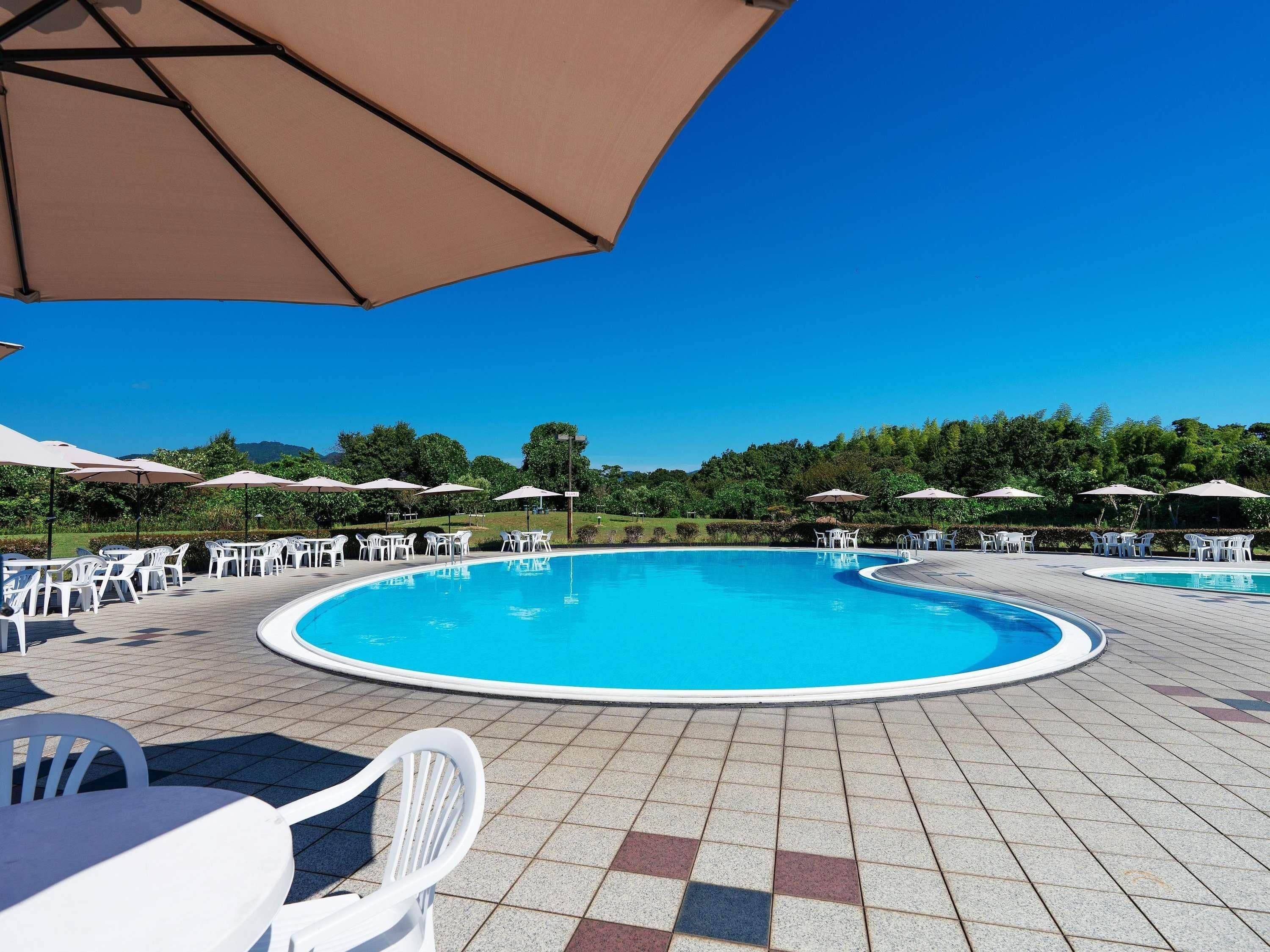 A swimming pool with surrounding white chairs and umbrellas, surrounded by greenery.