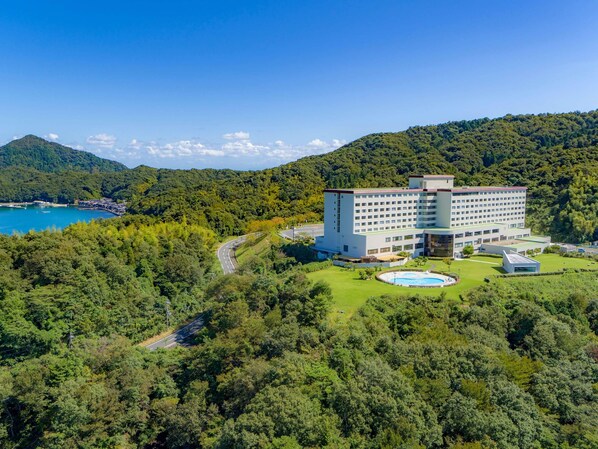Un hotel grande con varios pisos, rodeado de exuberante vegetación y una masa de agua.