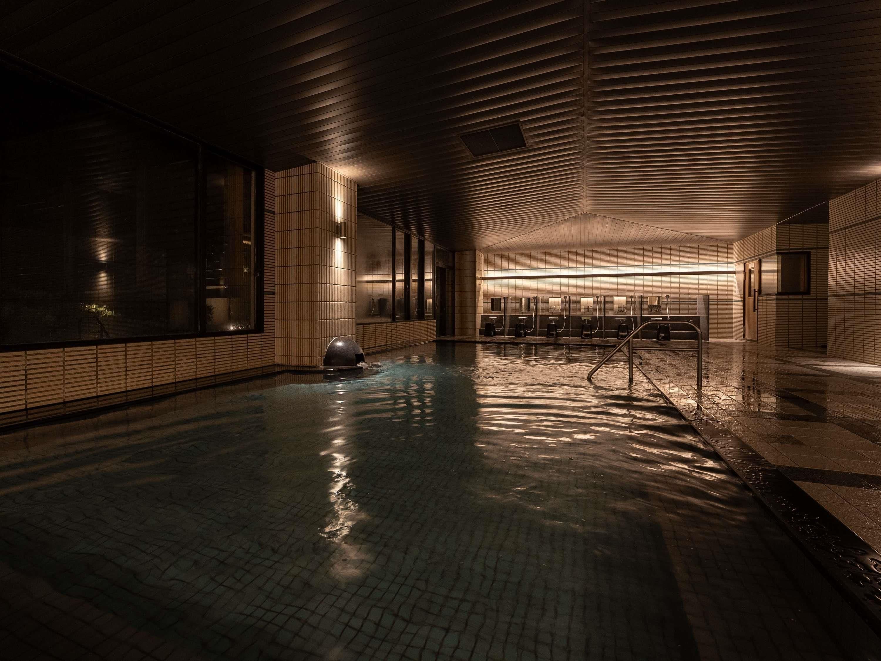 Une piscine intérieure avec des murs carrelés, un plafond en pente et une rangée de cabines d’habillage.