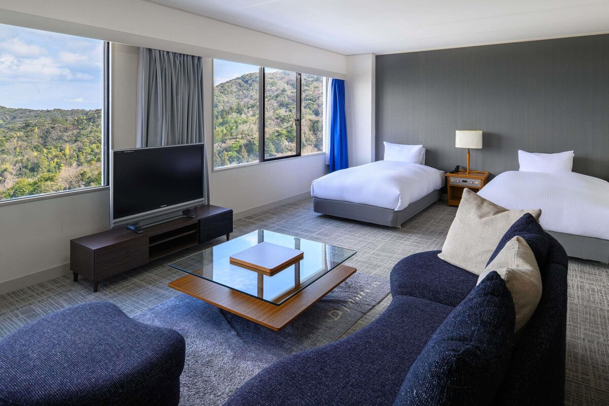 A hotel room with a bed, a TV, a sofa, and a glass coffee table.