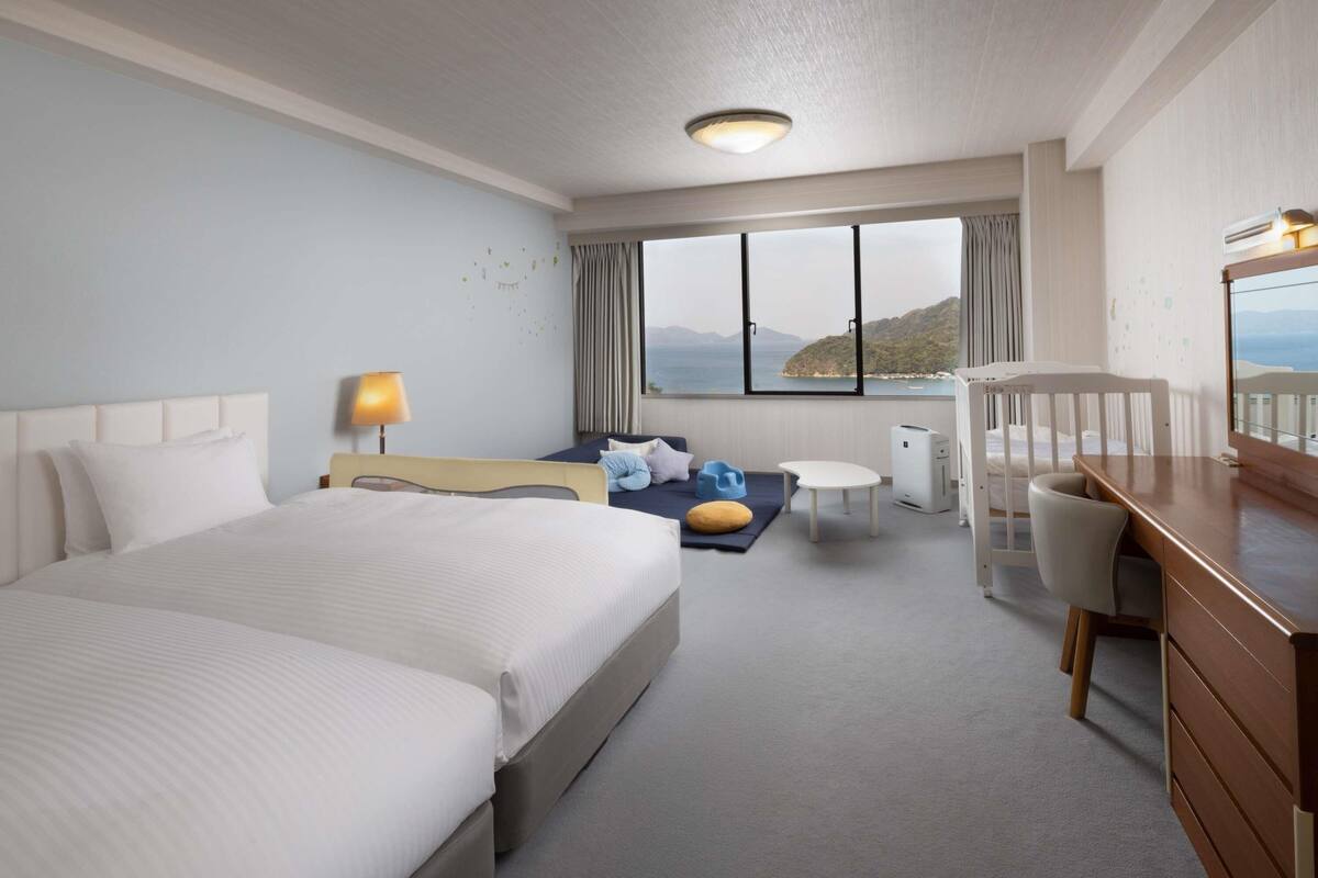 A hotel room with a large bed, a desk, a chair, a small table, and a view of the sea.