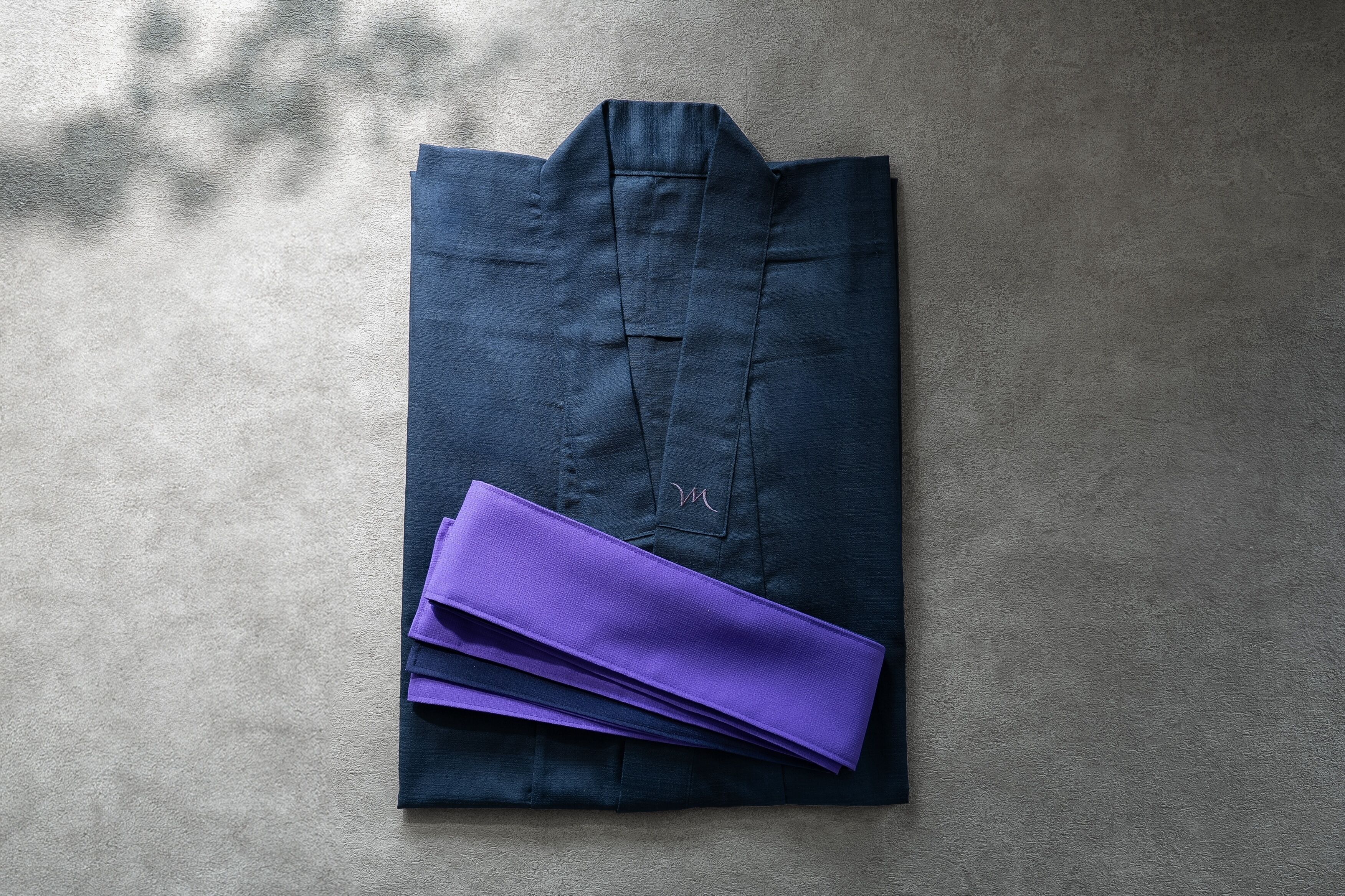 A neatly folded dark blue shirt with a purple pocket square on a textured grey surface.