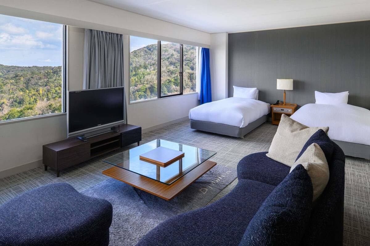 A hotel room with a bed, a TV, a sofa, and a glass coffee table.