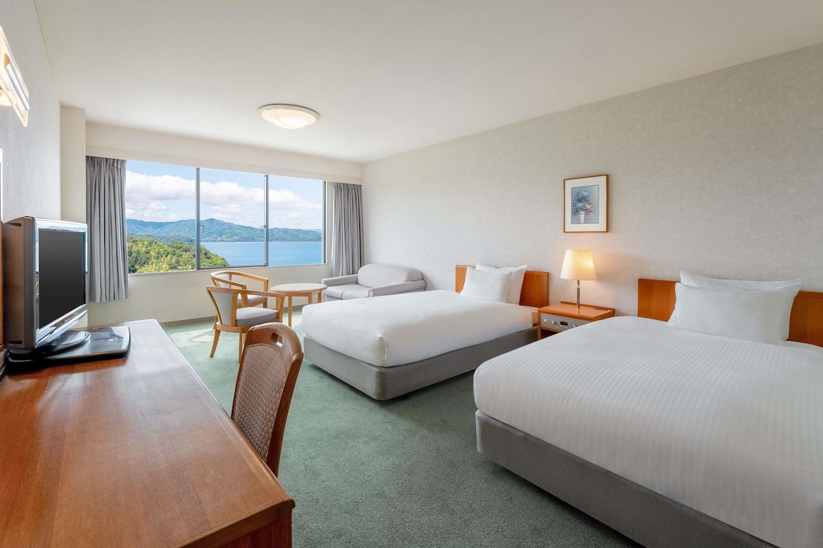 A hotel room with two beds, a desk, a TV, and a view of the mountains.