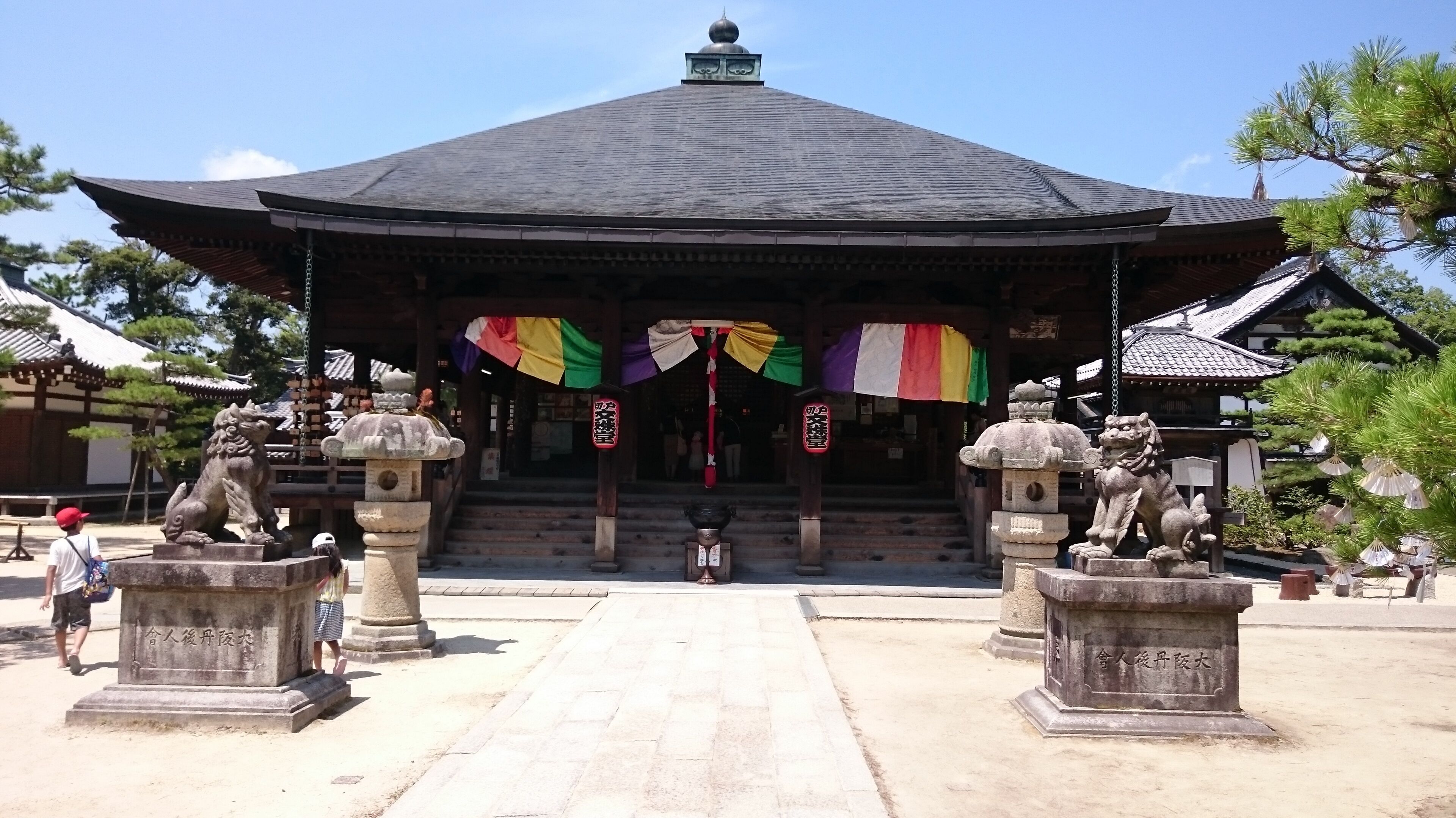 A traditional Japanese building with a tiled roof, stone lion statues, and a central entrance with colorful flags.