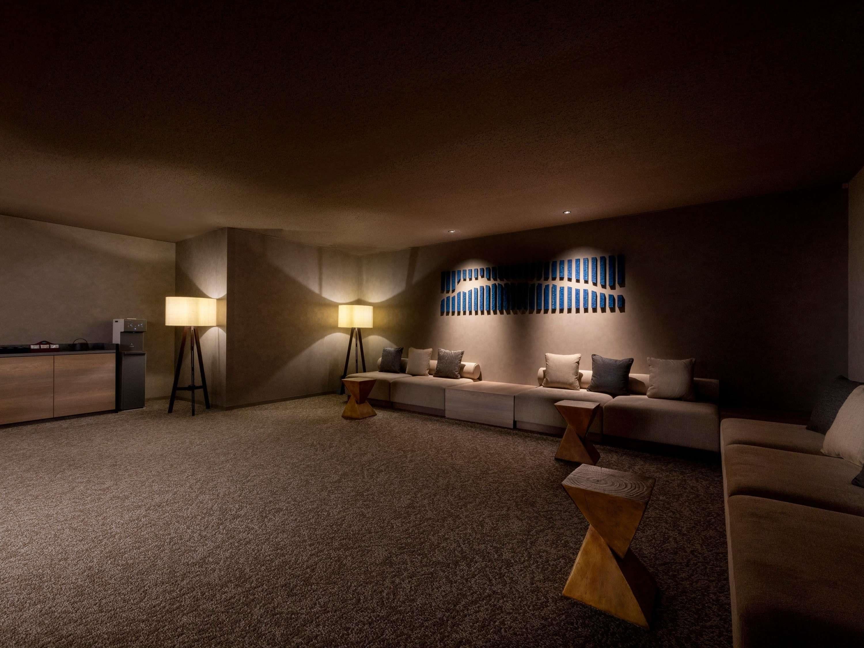 Een kamer in gedempt licht, met een bank, twee lampen en een wandlamp.