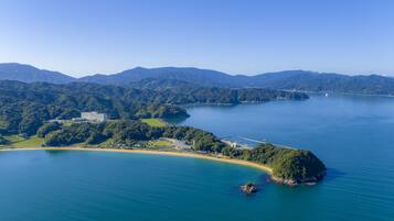 An aerial view of a coastal area with a large building, a small island, and surrounding mountains.