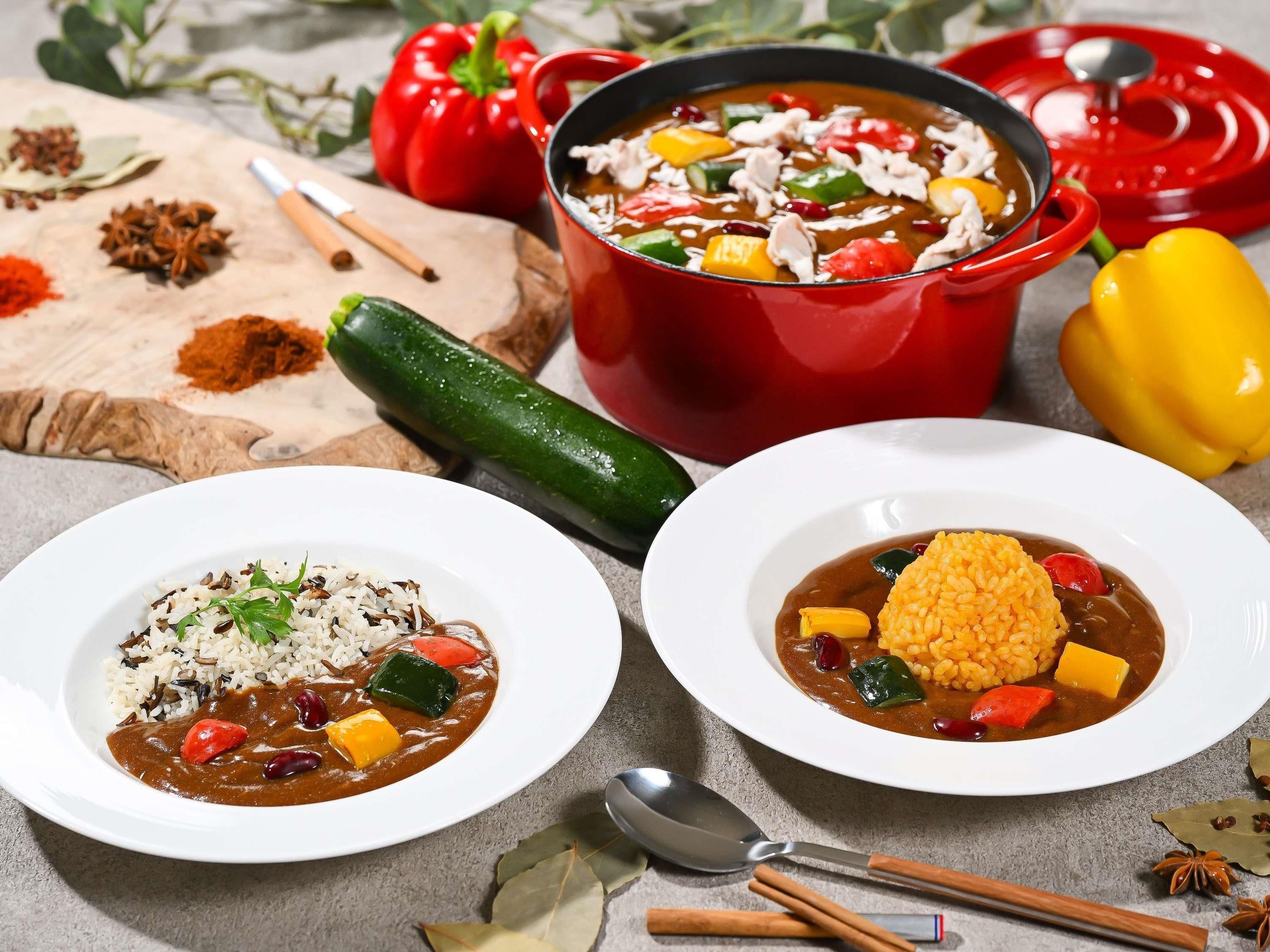 Deux bols de soupe contenant du riz et des légumes, une casserole rouge, ainsi que diverses épices et légumes disposés sur une table.