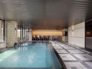 A modern indoor pool with tiled walls and a wooden ceiling.