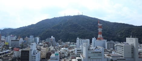 Un paisaje urbano costero con edificios modernos, una torre destacada y una montaña al fondo.