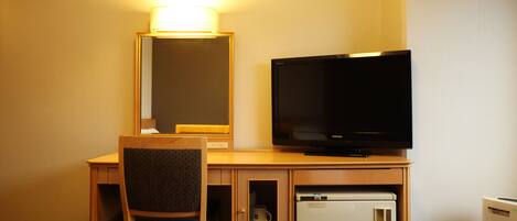 A hotel room with a wooden desk, a television, a small refrigerator, and a mirror.