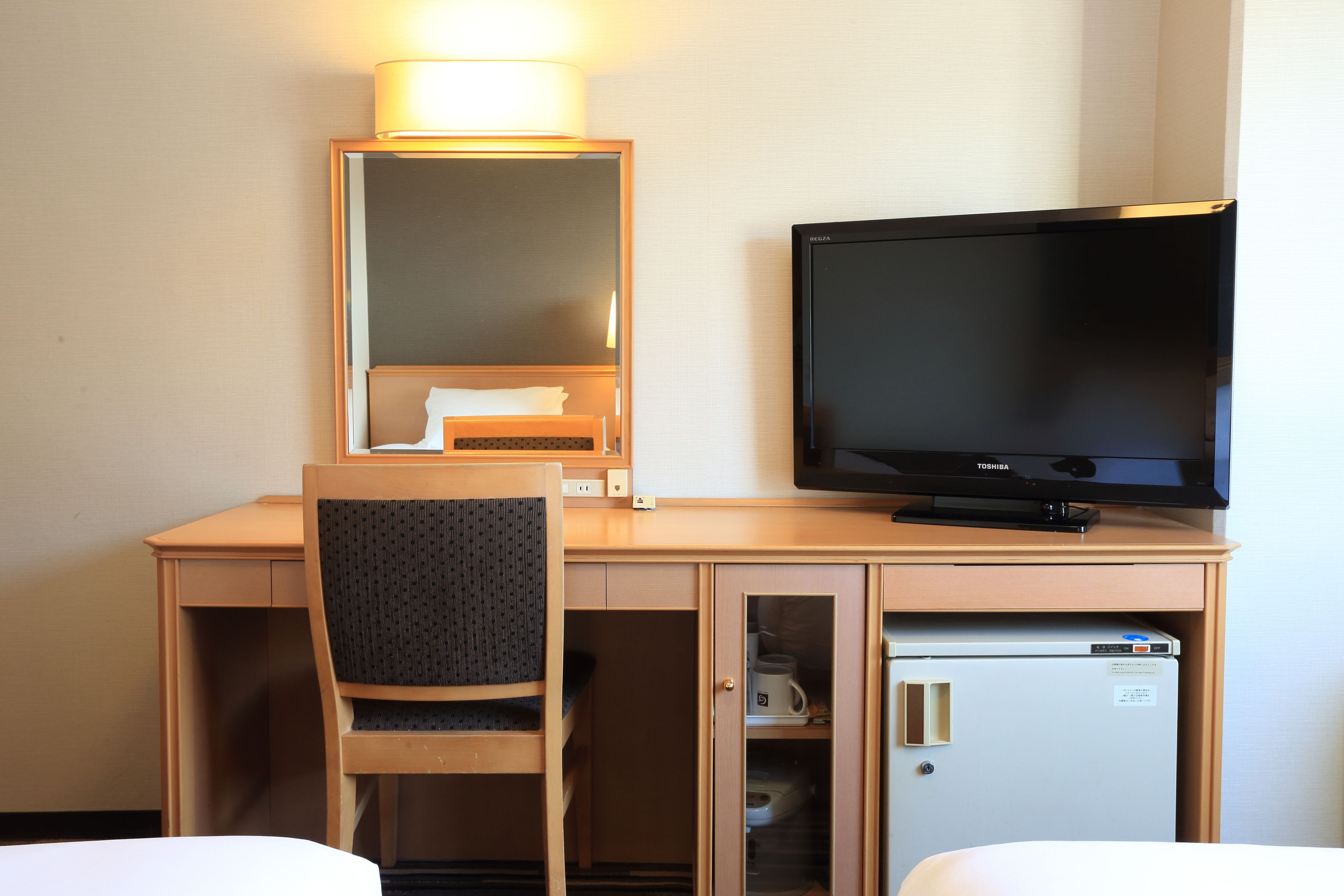 Habitación de hotel con escritorio de madera, televisor, silla y minibar.