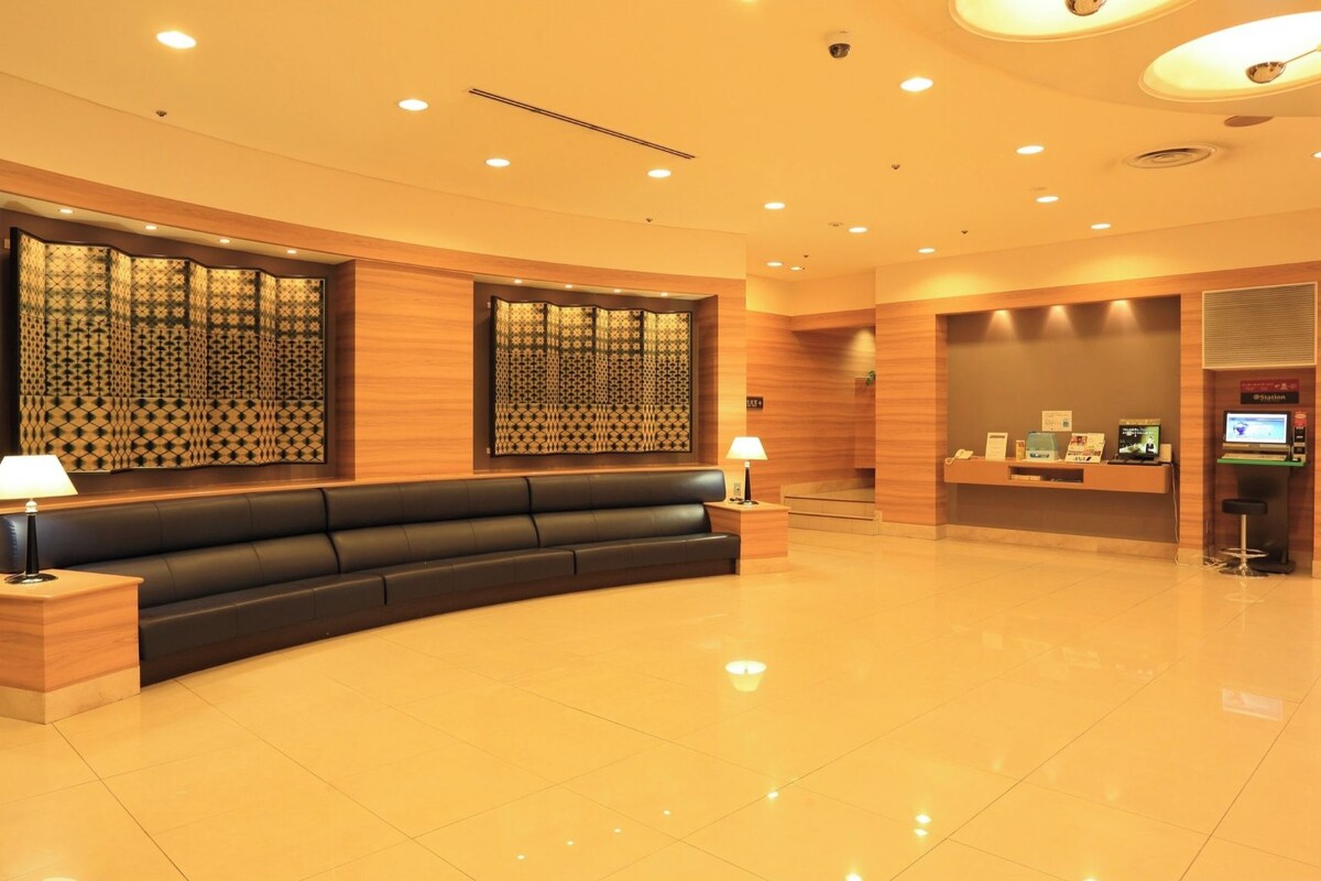 A modern reception area with a black leather sofa, wooden paneling, and a digital kiosk.