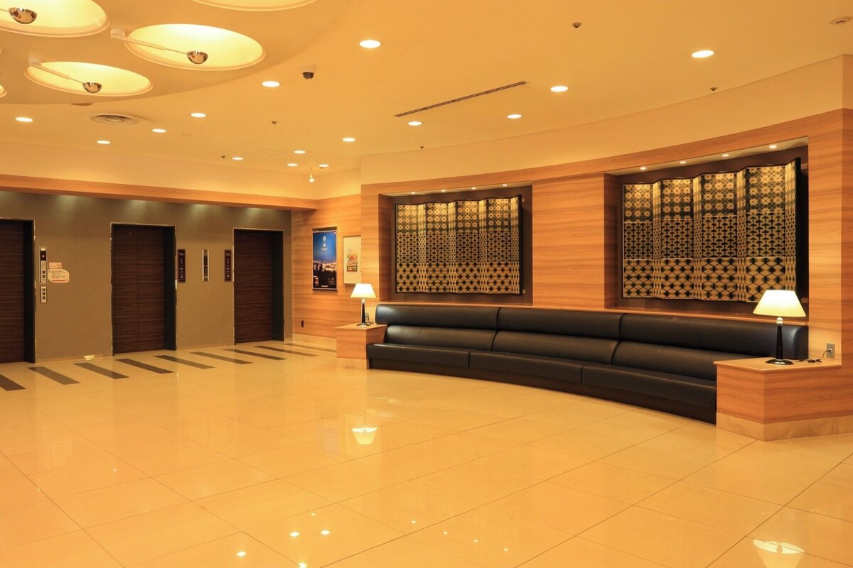 A modern hotel lobby with a reception desk, a black leather sofa, and a patterned wall.