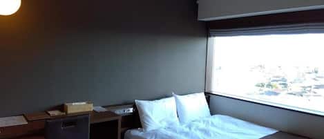 Hotellihuone, jossa on sänky, työpöytä, tuoli, ikkuna, josta on näkymä, ja riippuvalaisin.