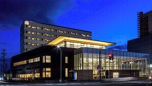 A modern building with a glass facade, a flat roof, and a prominent corner entrance. - Tsukino Hotel (Sakata)