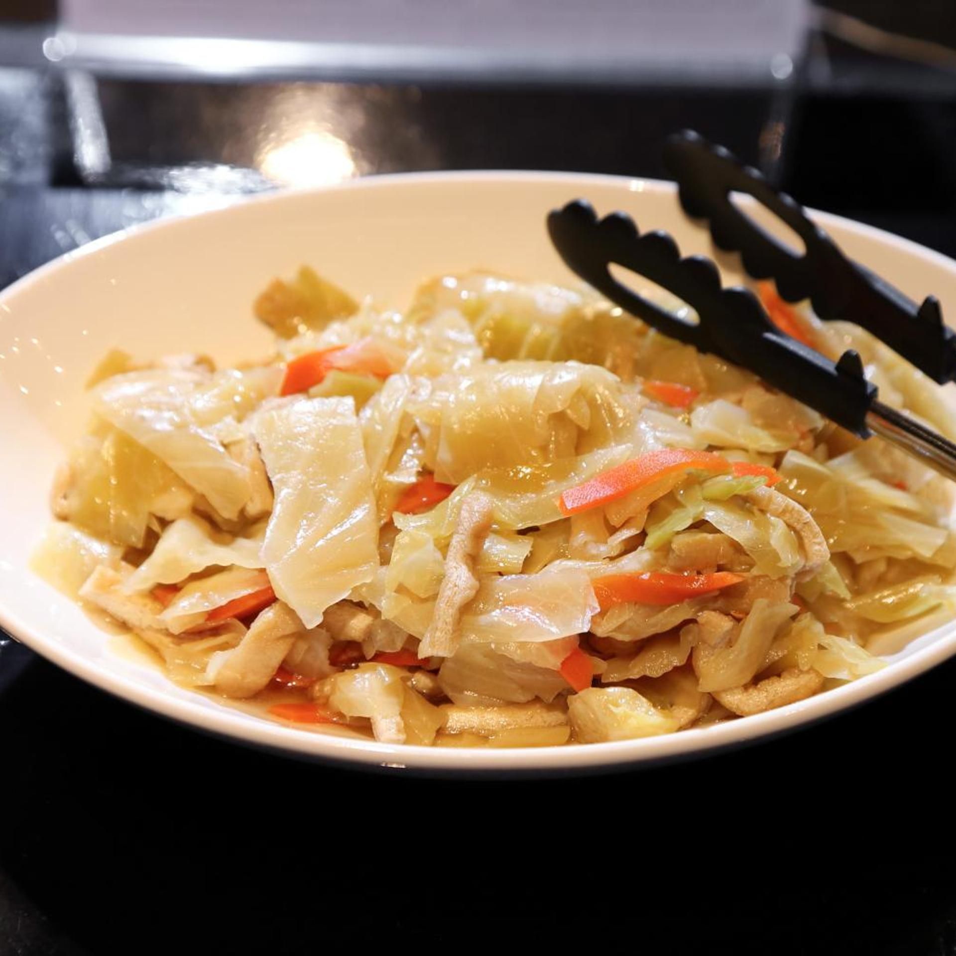 A bowl of cabbage and carrot stir-fry with tongs on the side.