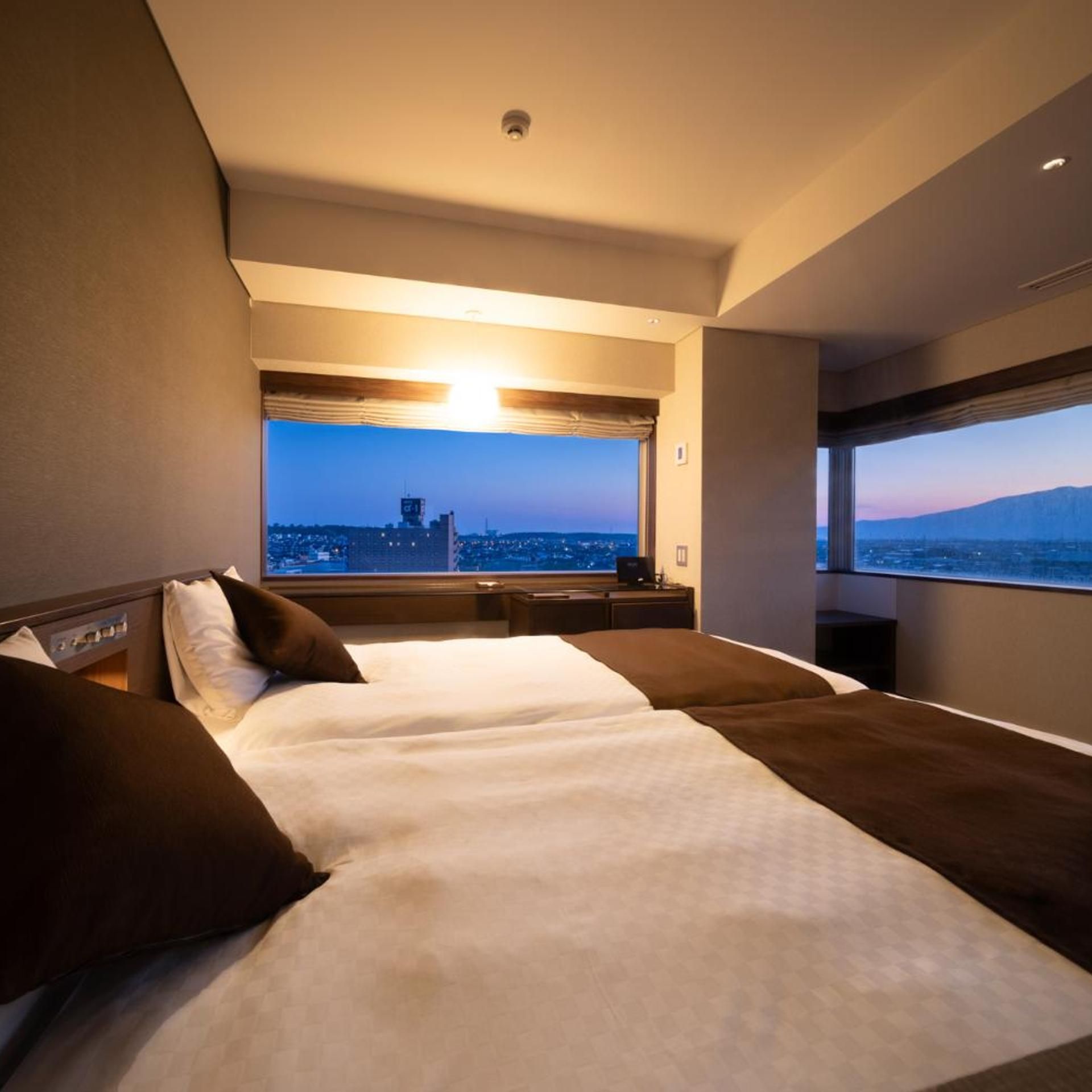 Une chambre d’hôtel avec un grand lit, une vue sur le paysage urbain et une fenêtre donnant sur les montagnes.