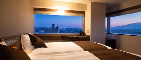 Habitación de hotel con una cama grande, vista a la ciudad y ventana con vistas a las montañas.