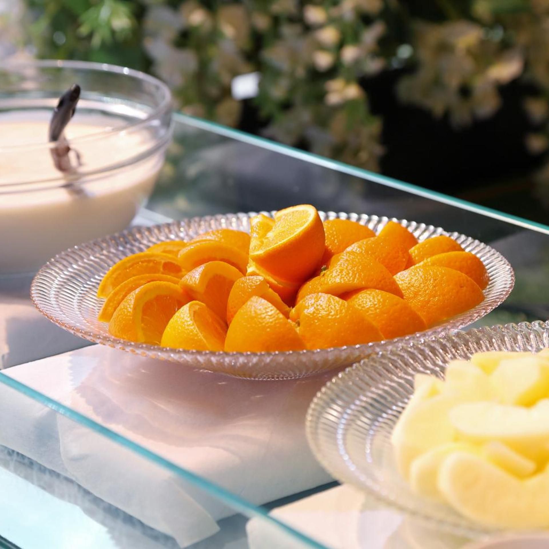 A glass table with a plate of sliced oranges and a bowl of cream.