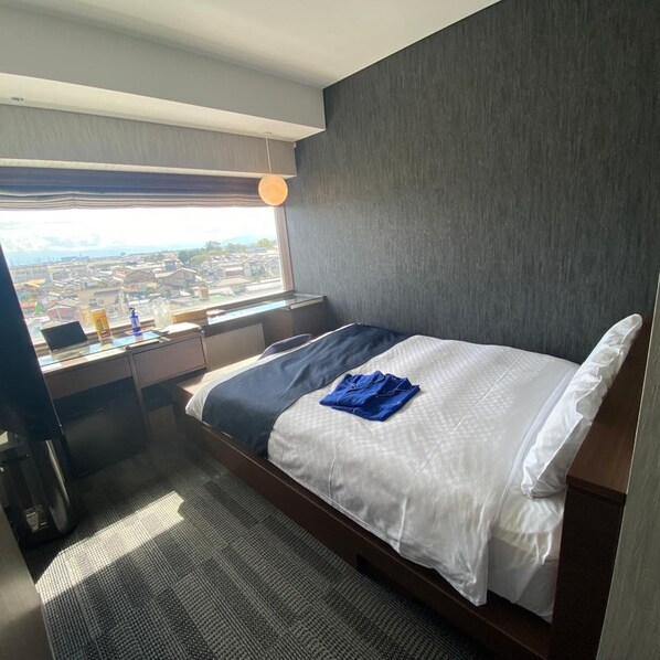 A hotel room with a bed, a desk with a computer, and a view of the city. - Tsukino Hotel (Sakata)