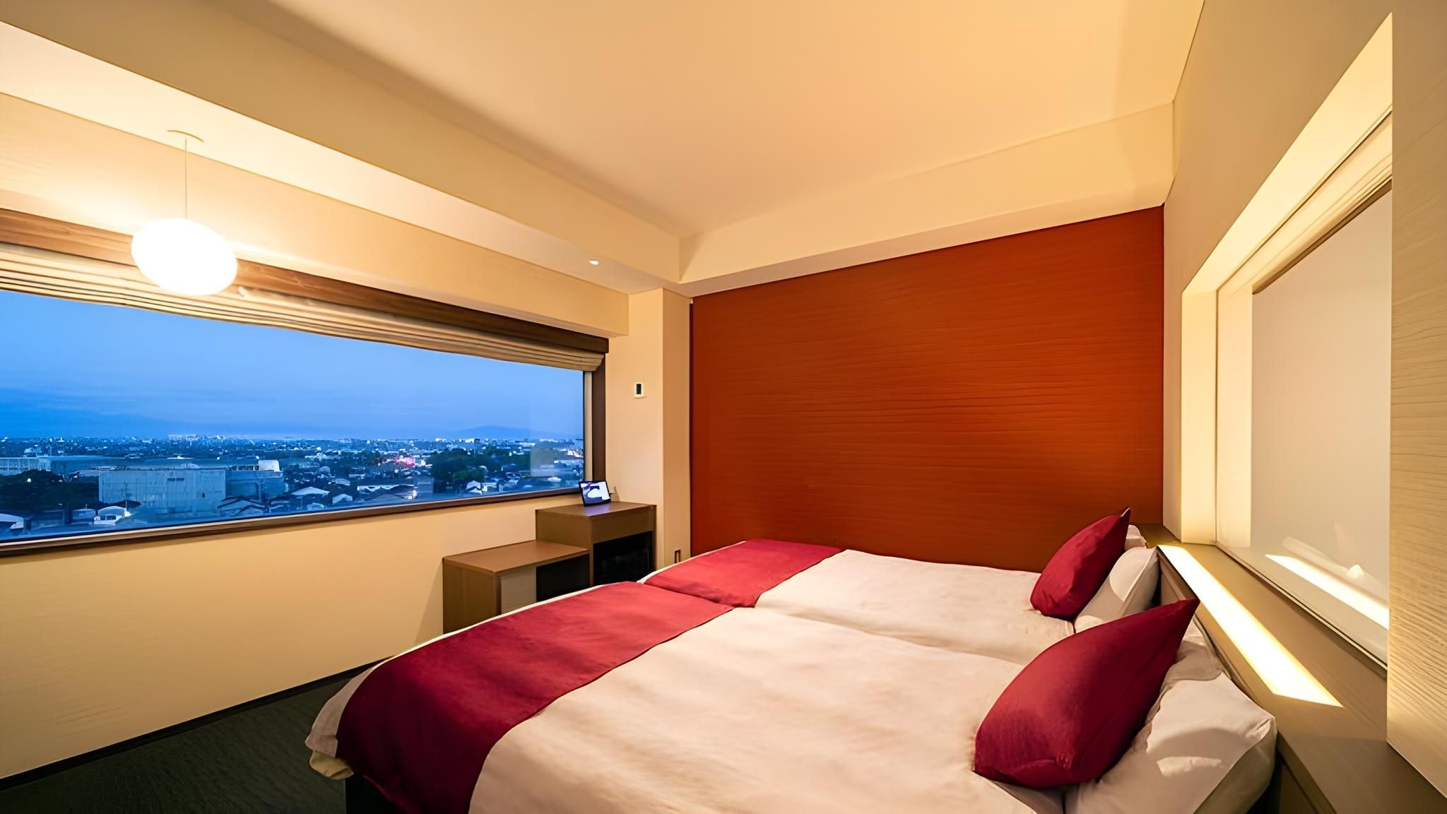A hotel room with a large bed, a desk, and a window with a city view.