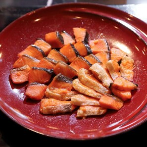 A red plate with sliced carrots and a dark liquid, possibly a sauce. - Tsukino Hotel (Sakata)