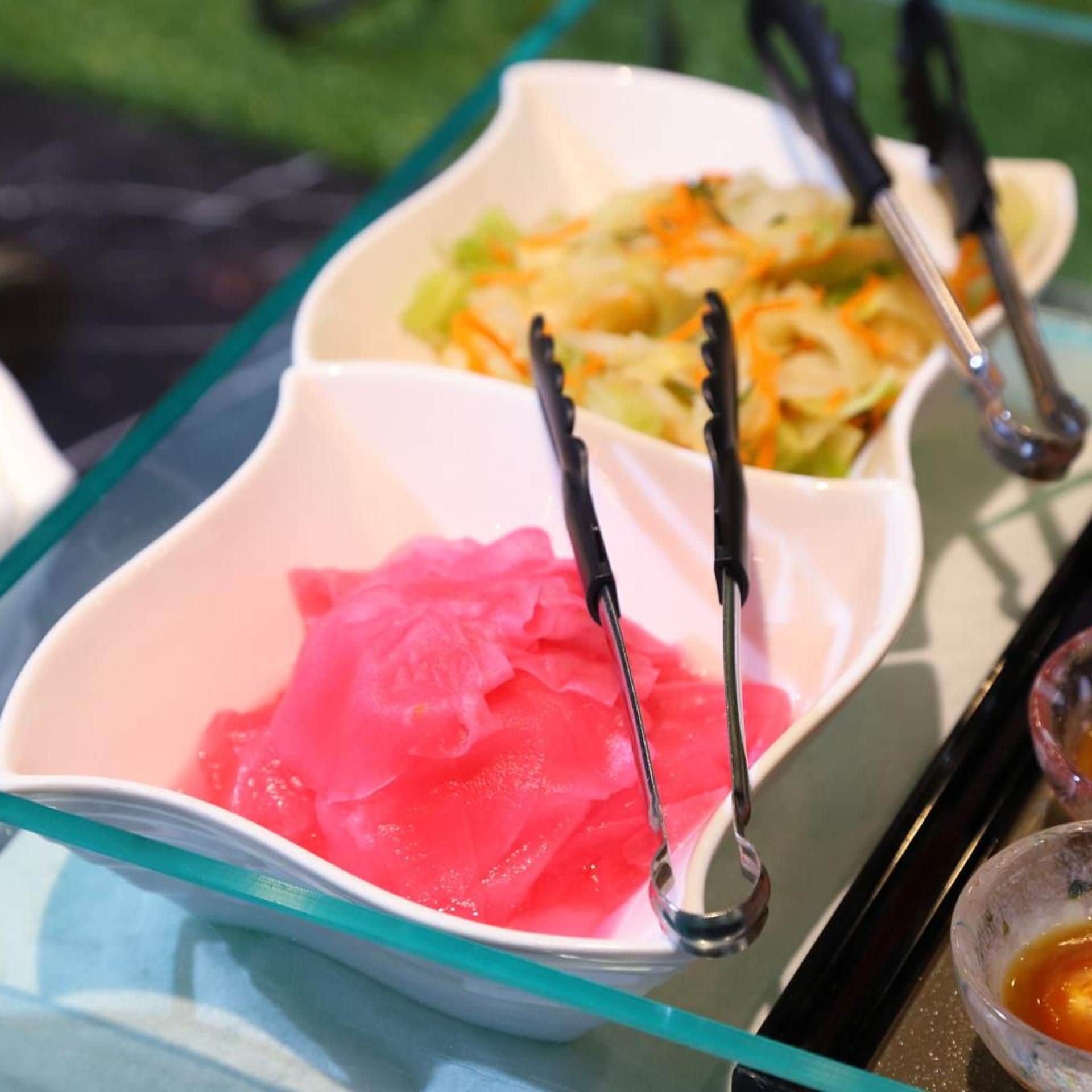 A table with three bowls of food, each with a pair of tongs.