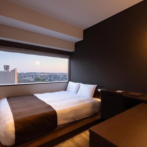 A hotel room with a large window, a bed, a desk, and a chair.