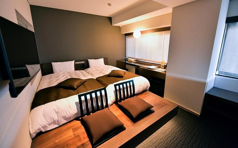A modern bedroom with a bed, bedside tables, a desk, and a window.