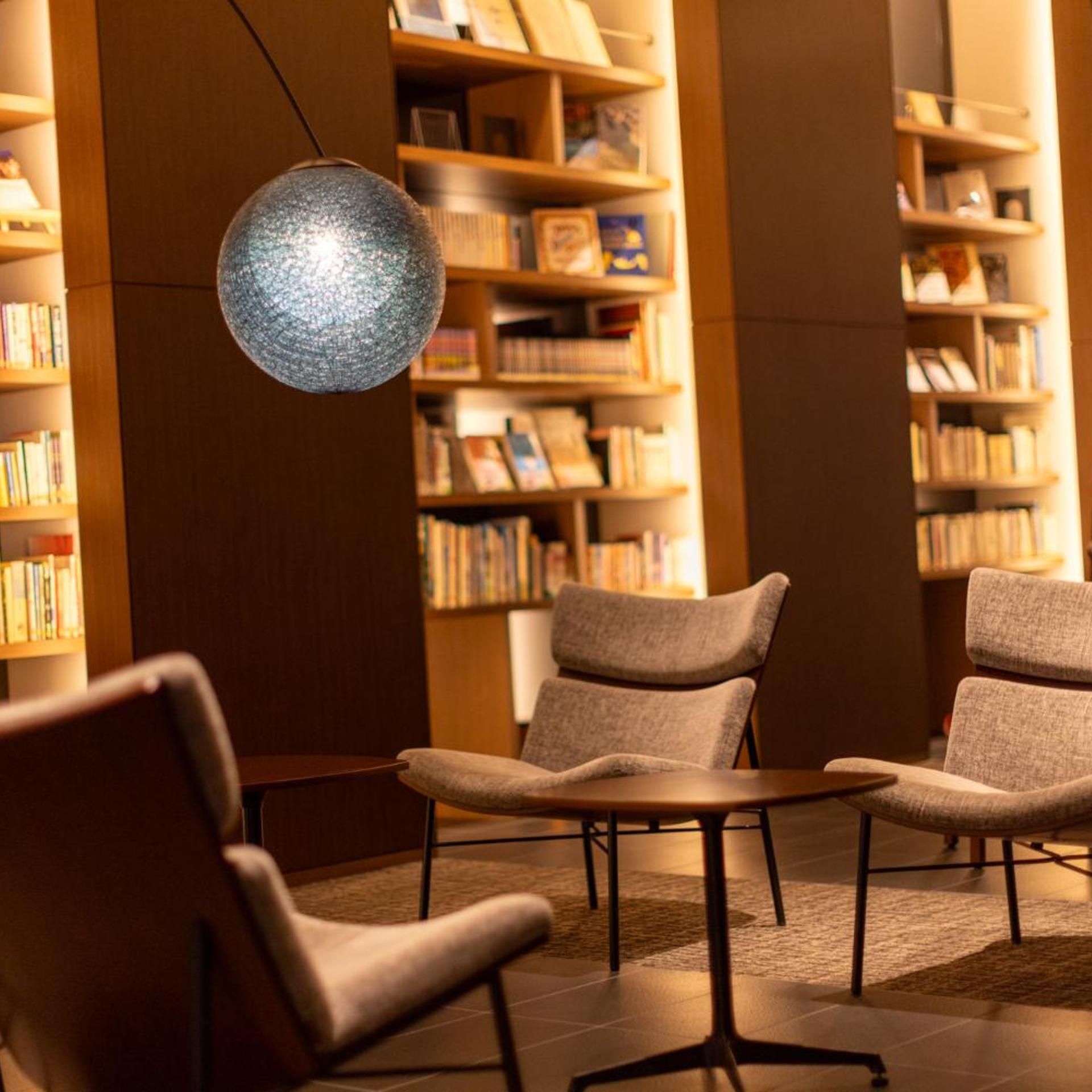 A library reading area with bookshelves, comfortable seating, and a decorative light fixture.