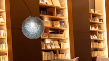 A library reading area with bookshelves, comfortable seating, and a decorative light fixture.