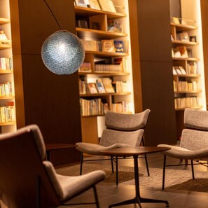 A library reading area with bookshelves, comfortable seating, and a decorative light fixture. - Tsukino Hotel (Sakata)