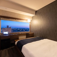 Habitación de hotel con cama, escritorio y un ventanal con vista a la ciudad.
