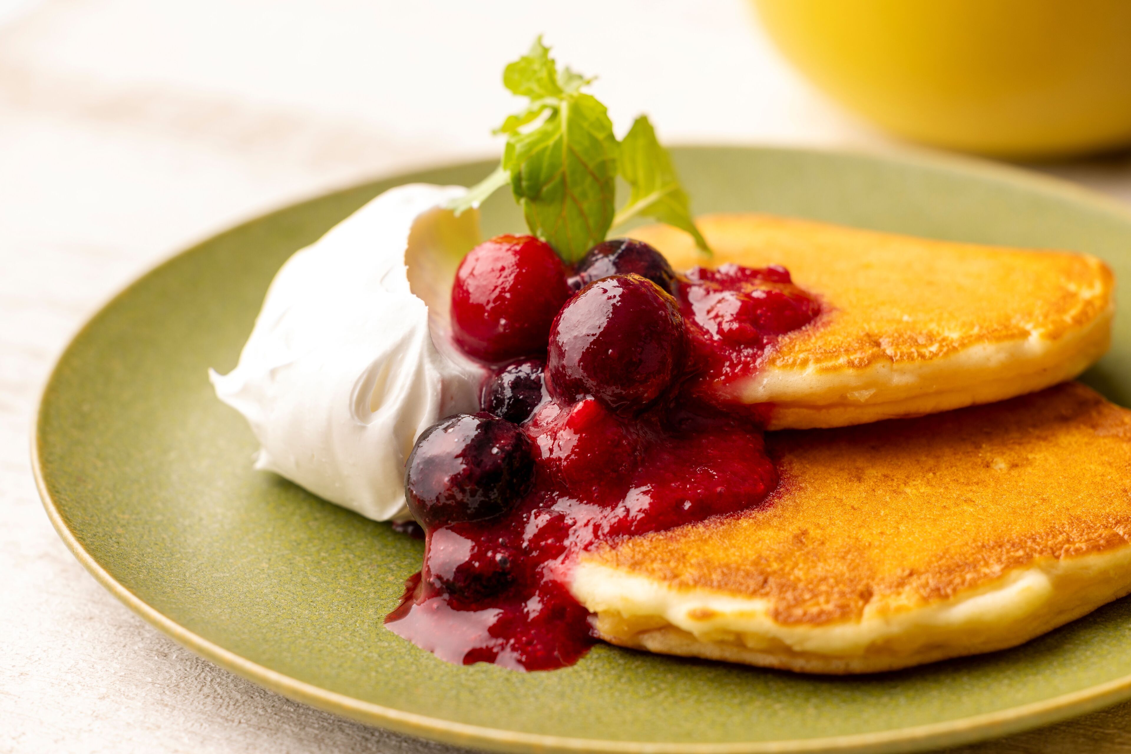 A plate with pancakes topped with blueberries and a dollop of cream.