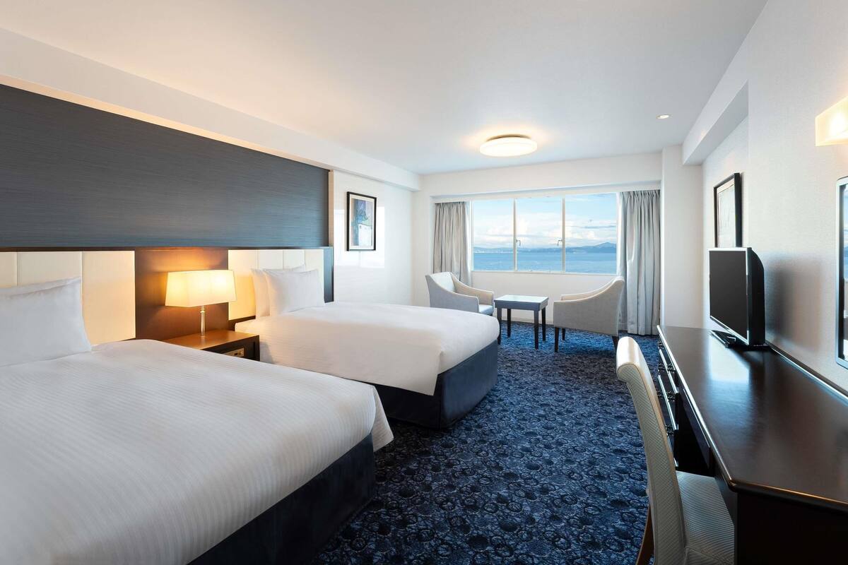 Een hotelkamer met twee bedden, een bureau, een televisie en uitzicht op zee.