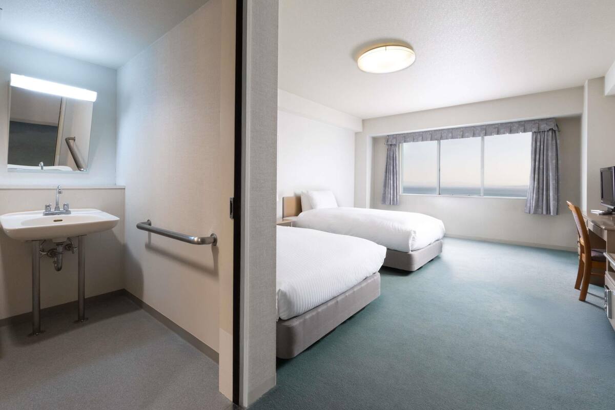 Hotelkamer met een bed, bureau, stoel, televisie en een badkamer met wastafel en spiegel.