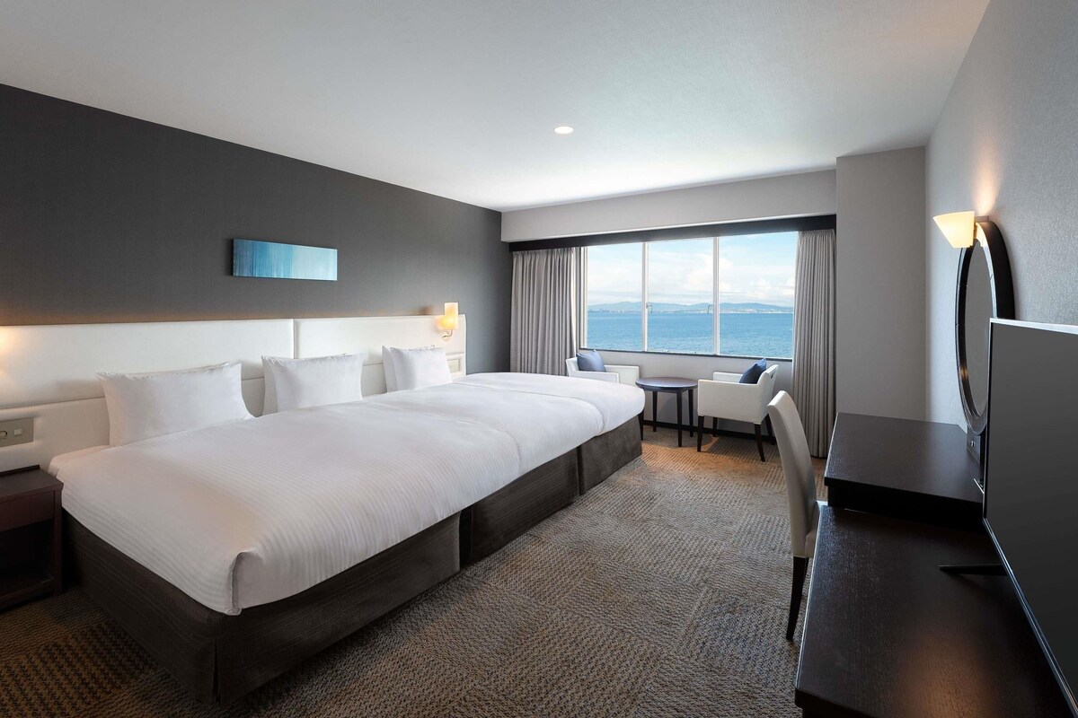Habitación de hotel moderna con una cama grande, un escritorio y vistas al mar.