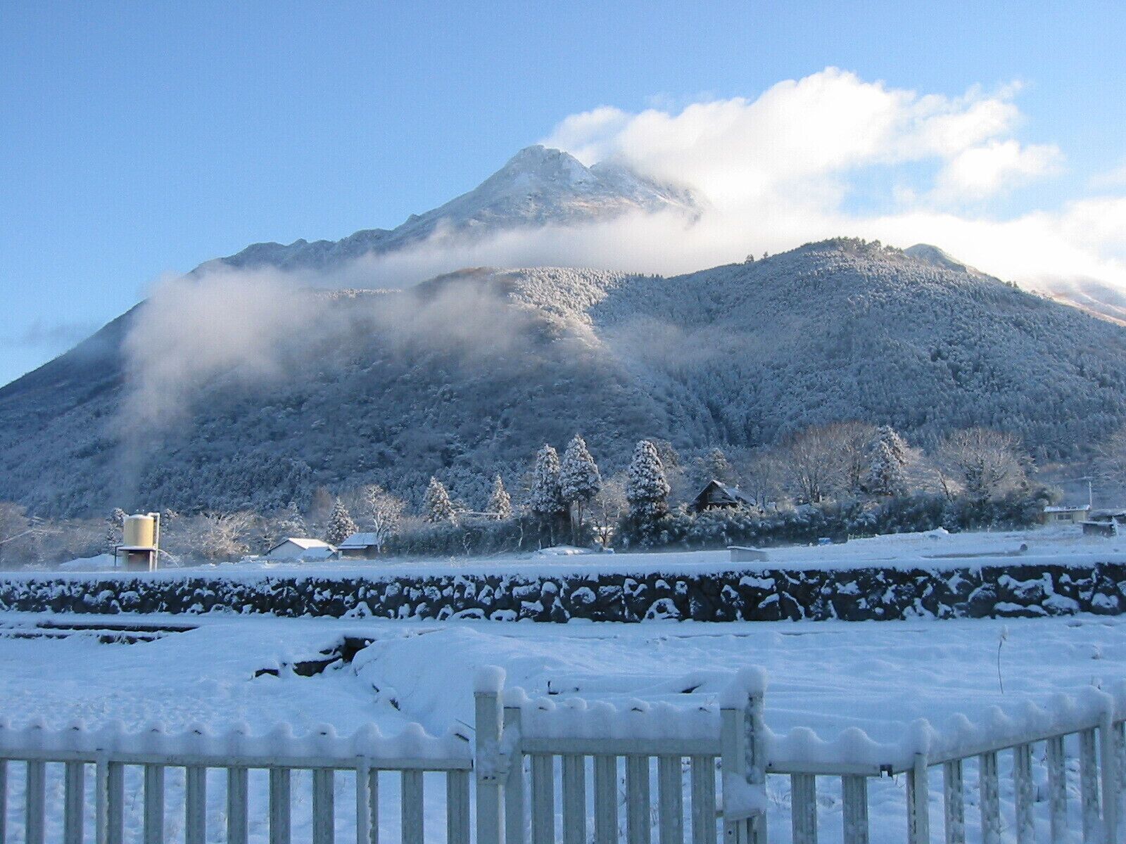 Un paysage enneigé avec une montagne, une clôture en bois et un mur de pierres.