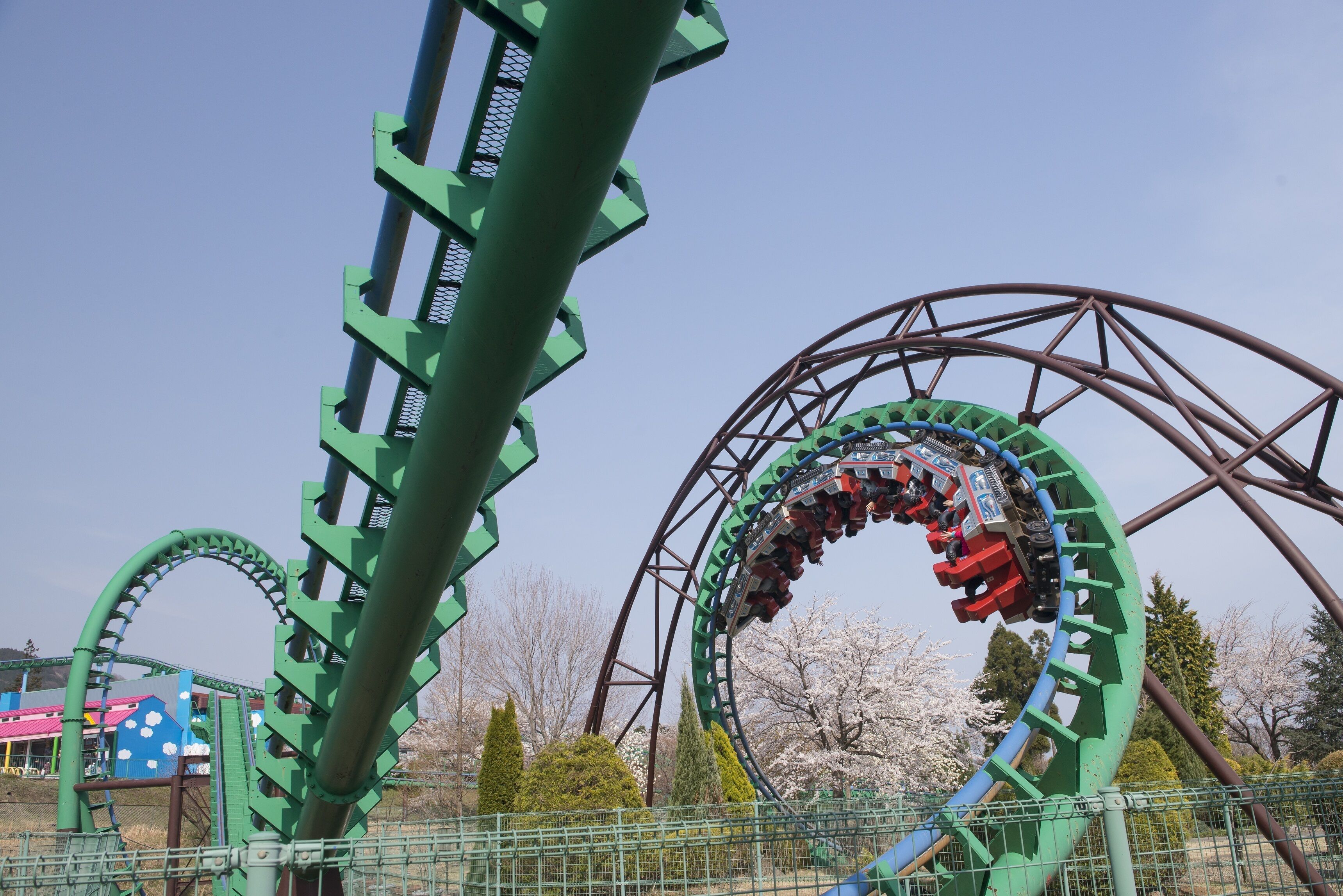 Een achtbaan met een groene baan en stalen constructie, omringd door bomen en een heldere lucht.