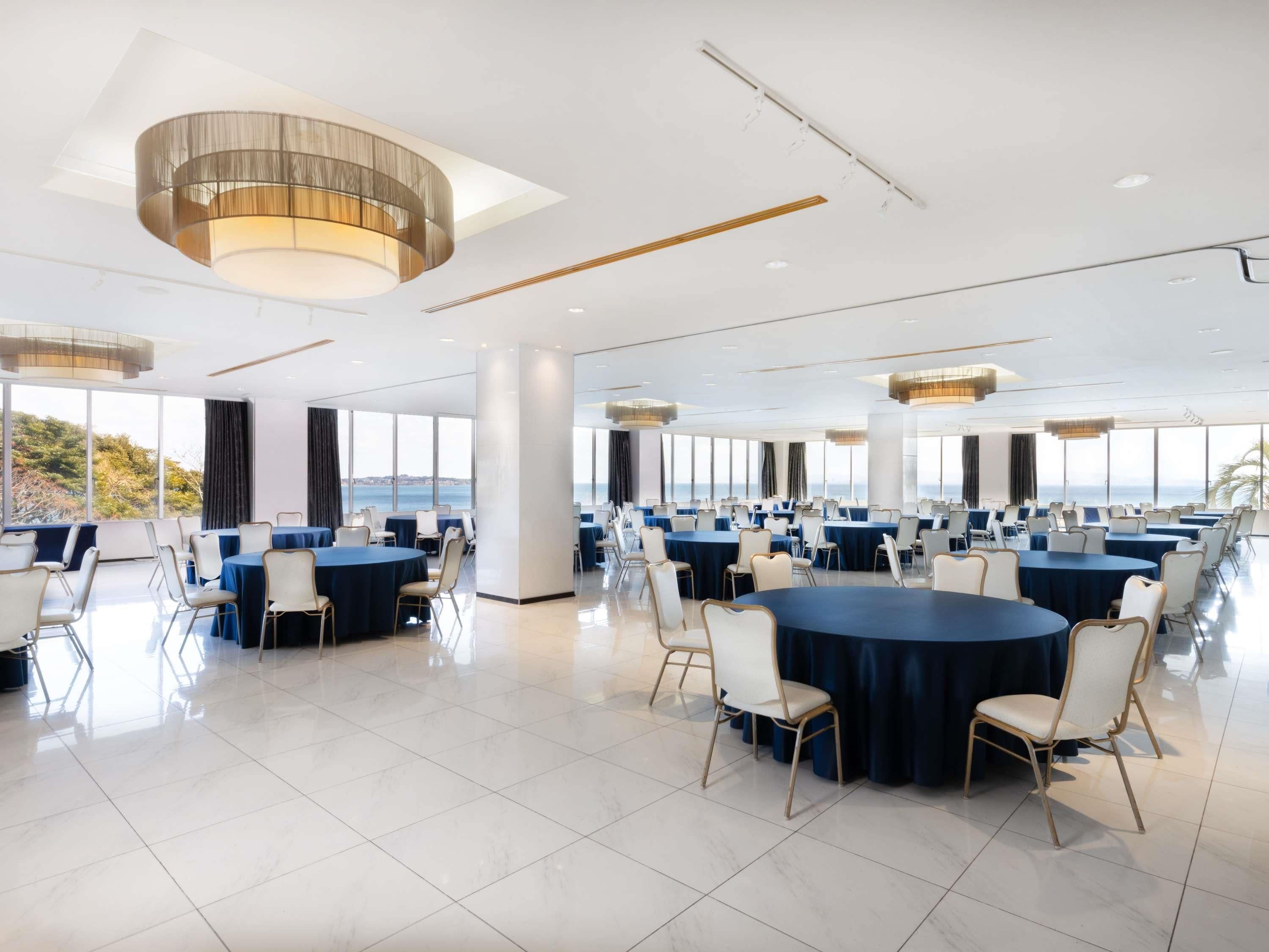 A spacious conference room with round tables and chairs, large windows with a view, and modern lighting fixtures.