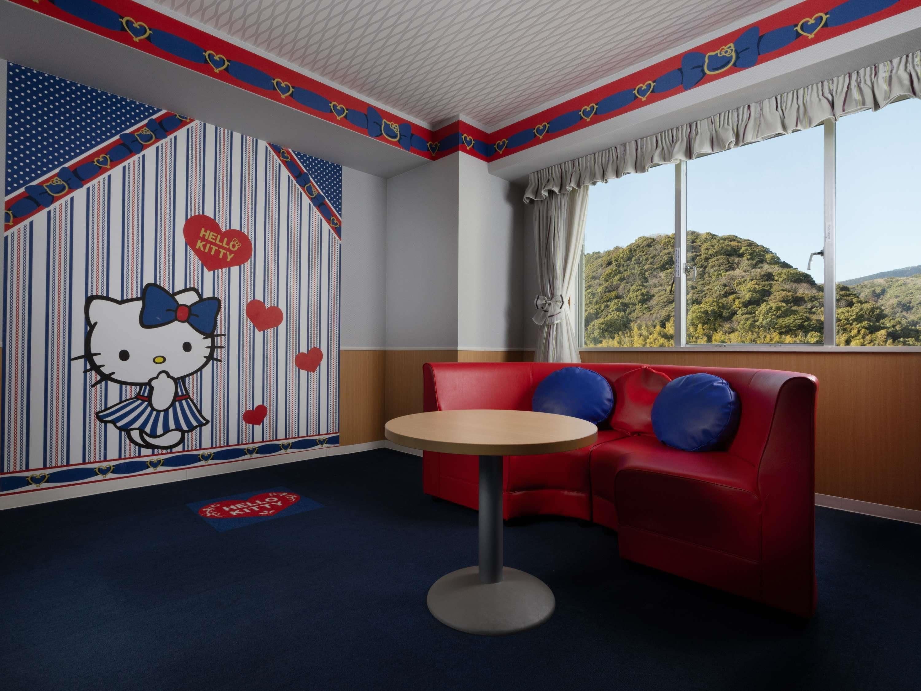 A room with a red sofa, a round table, and a wall with Hello Kitty decorations.