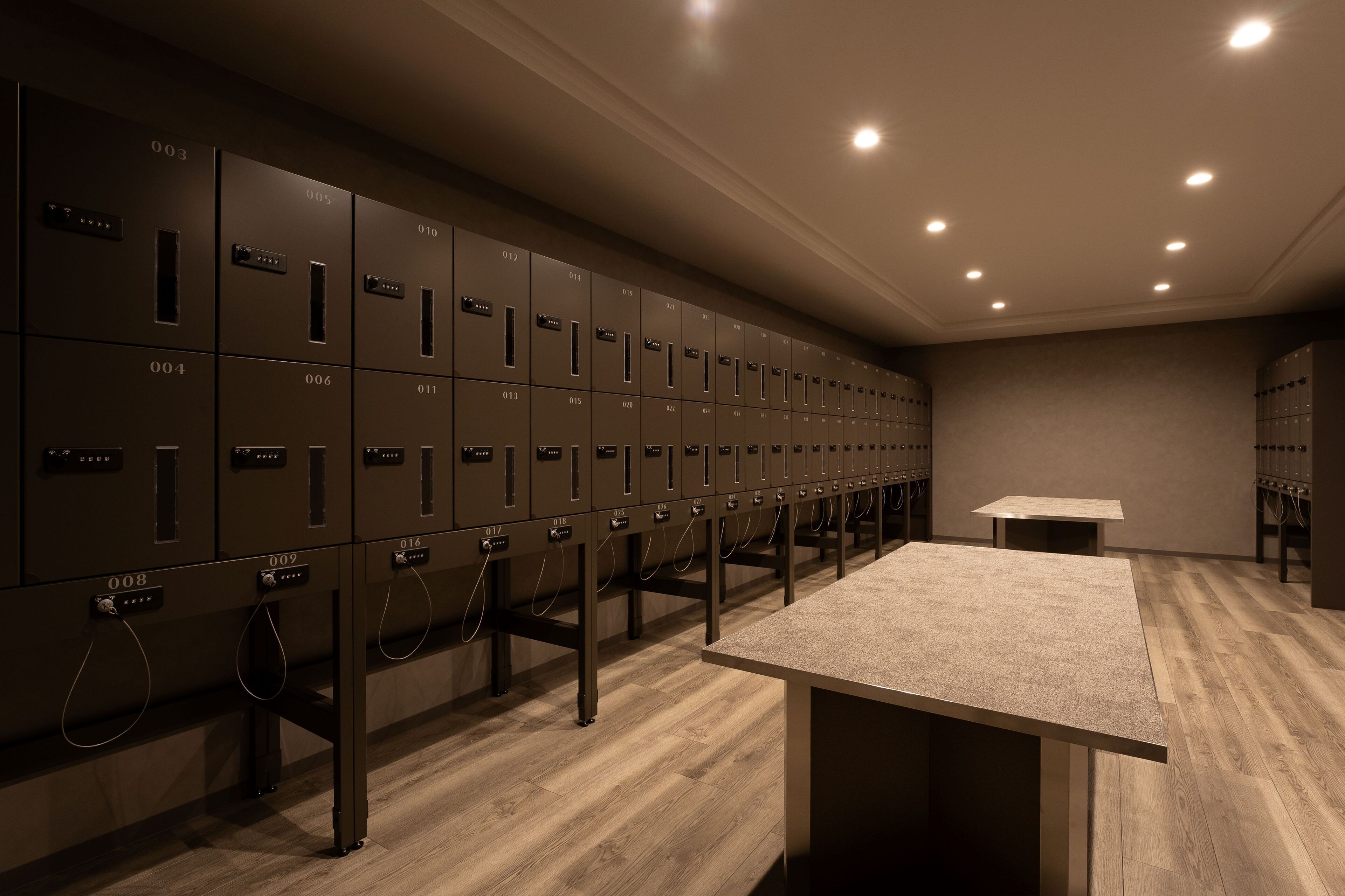 A row of metal lockers with numbers on them, a table, and a carpeted floor.